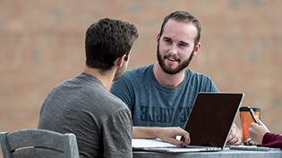 Two men talking and studying together outside.